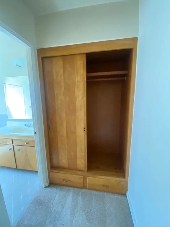 Bedroom closet with wooden doors and drawers; bathroom vanity visible in adjacent doorway.