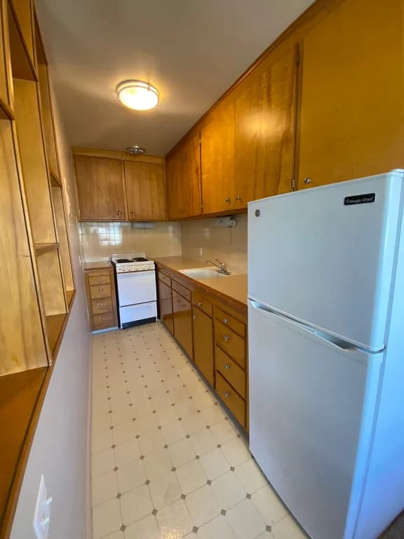 Galley kitchen with wooden cabinets, a white stove, a white Magic Chef refrigerator, and patterne...