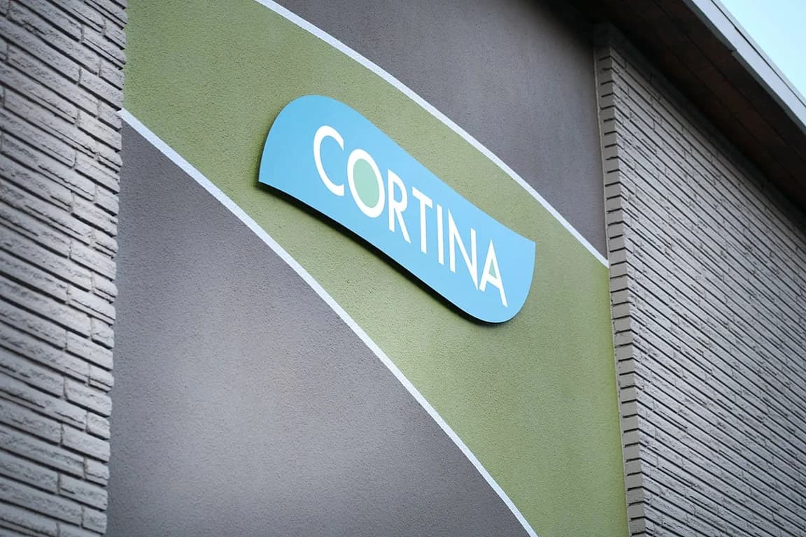 Blue Cortina Apartments sign on a modern building exterior with green and gray textures.
